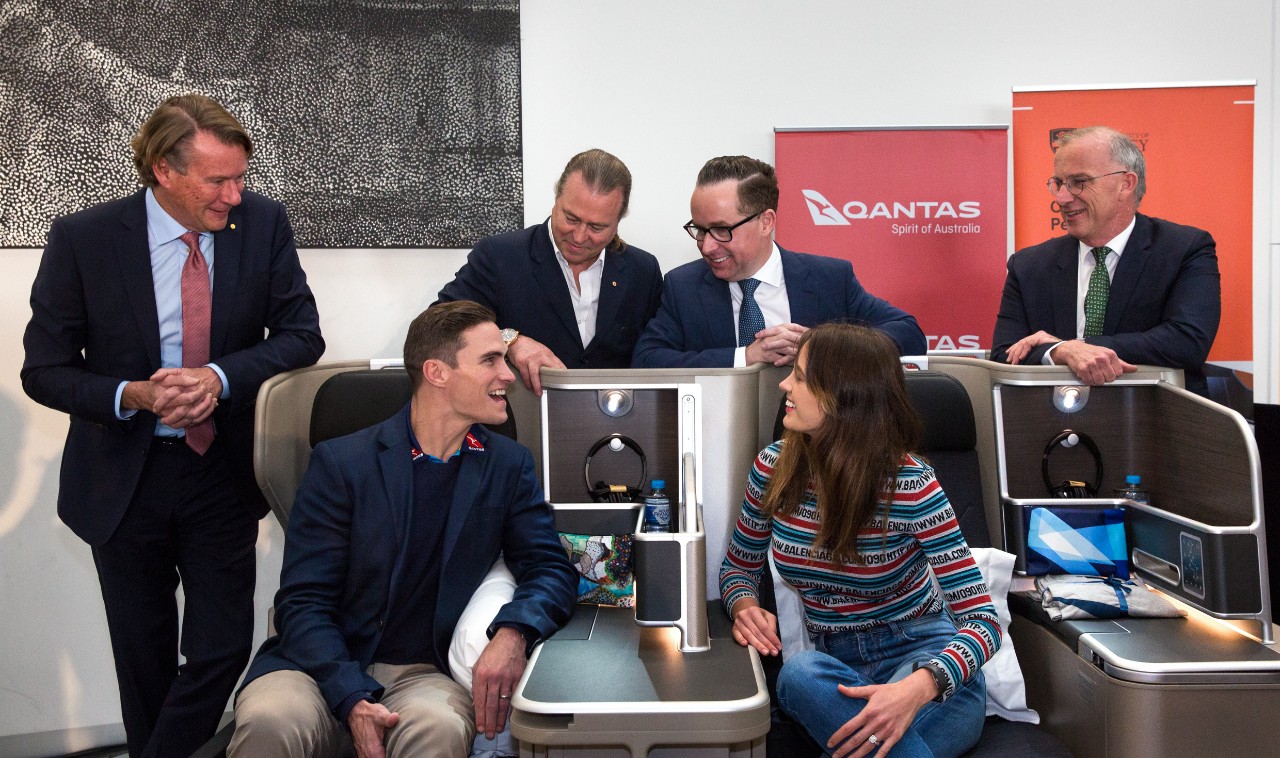A photo of a group of people standing and sitting around aeroplane seats.