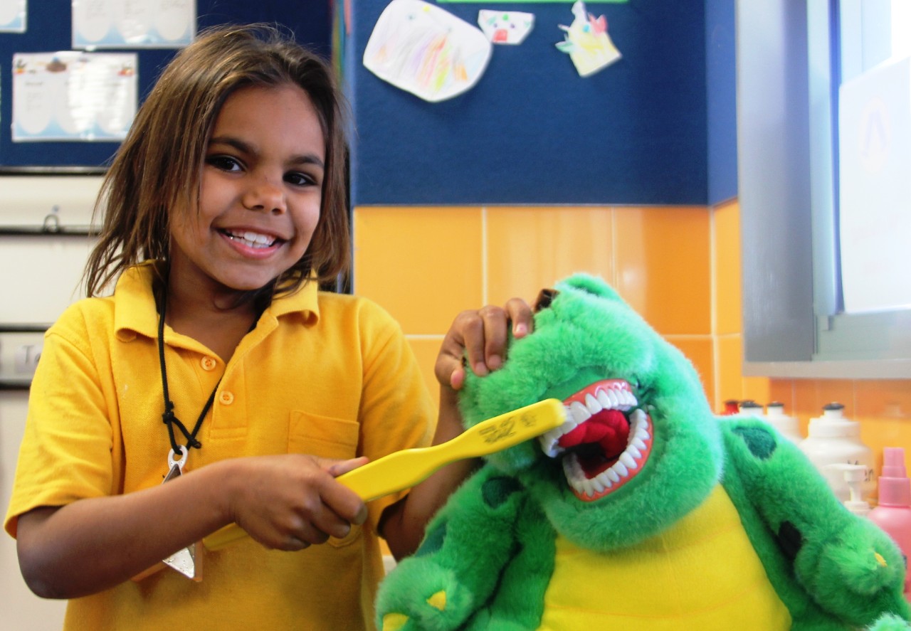 A young girl brushing the teeth of a stuffed toy.