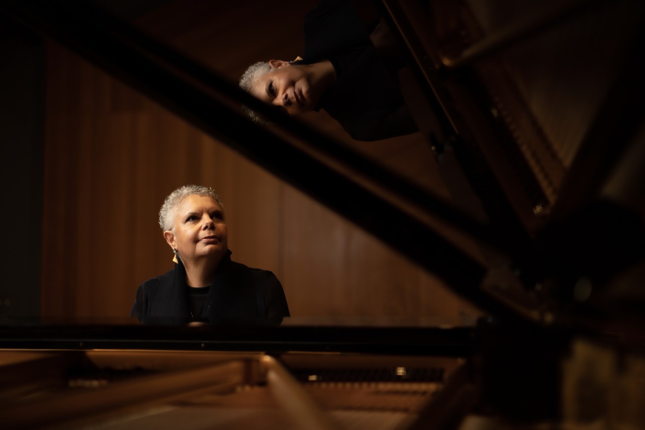 Deborah behind a black grand piano, sitting and looking to the side