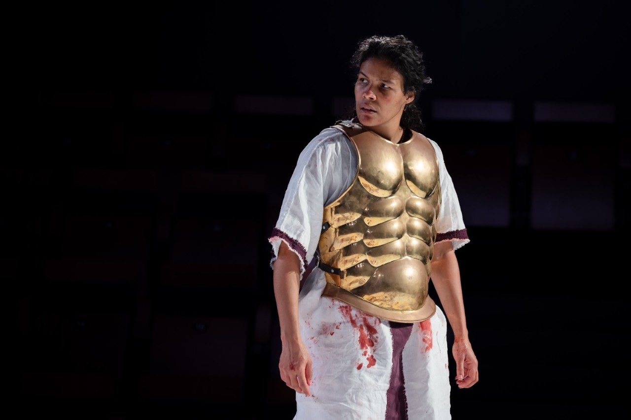 photo of female actor Zahra Newman on stage in Julius Caesar. She is playing Brutus wearing a golden breastplate over a toga. 