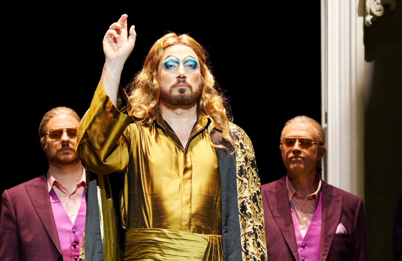 A male singer dressed all in gold raises his arm