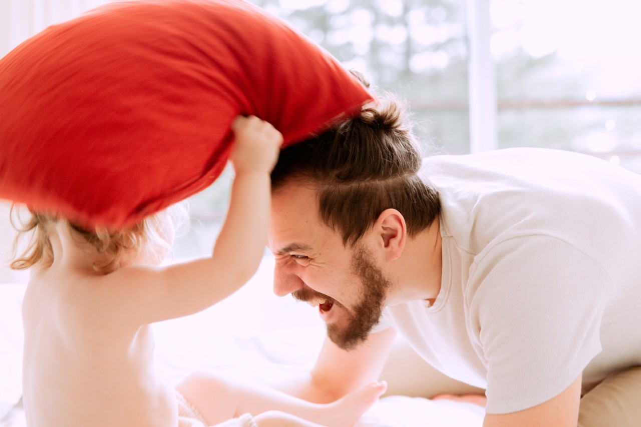 Photo of a dad having a pillow fight with a little girl