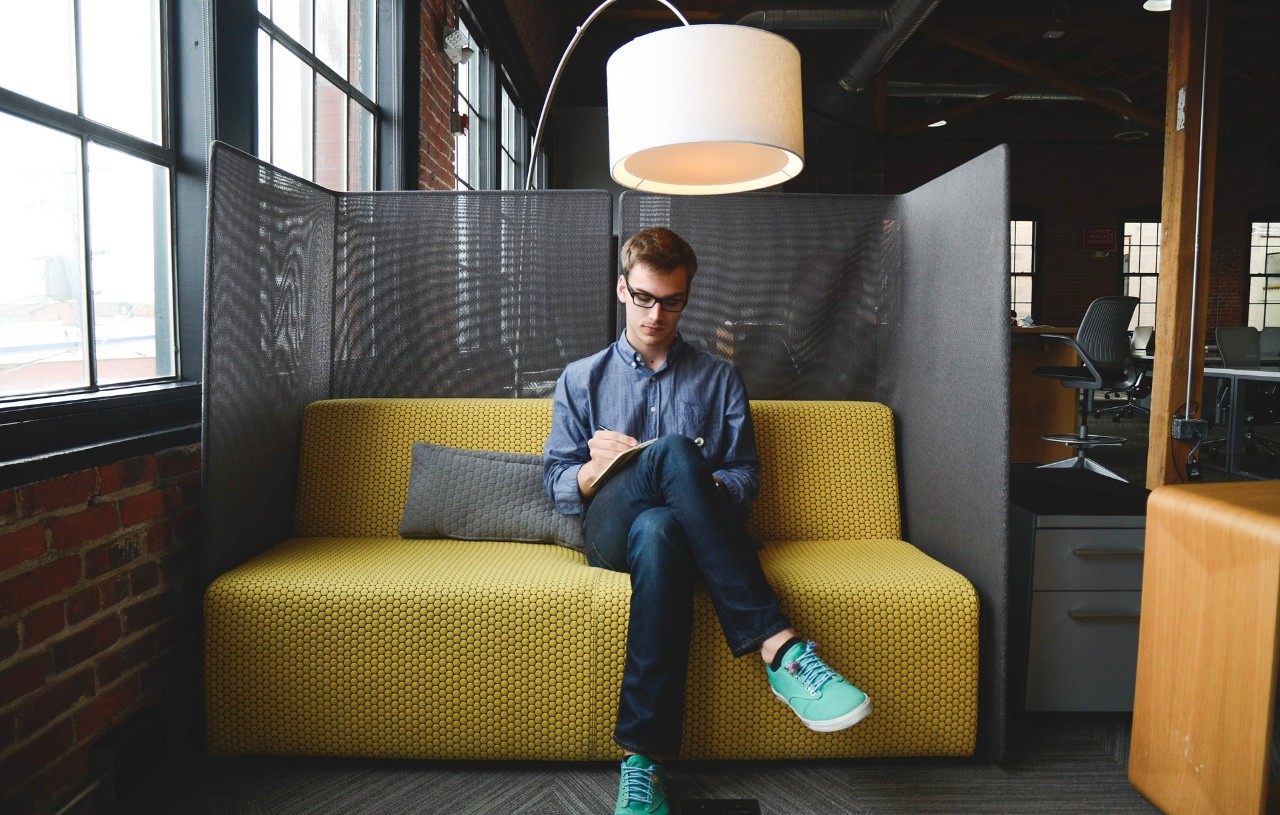 A young entrepreneur sits at on a chair writing down notes. 