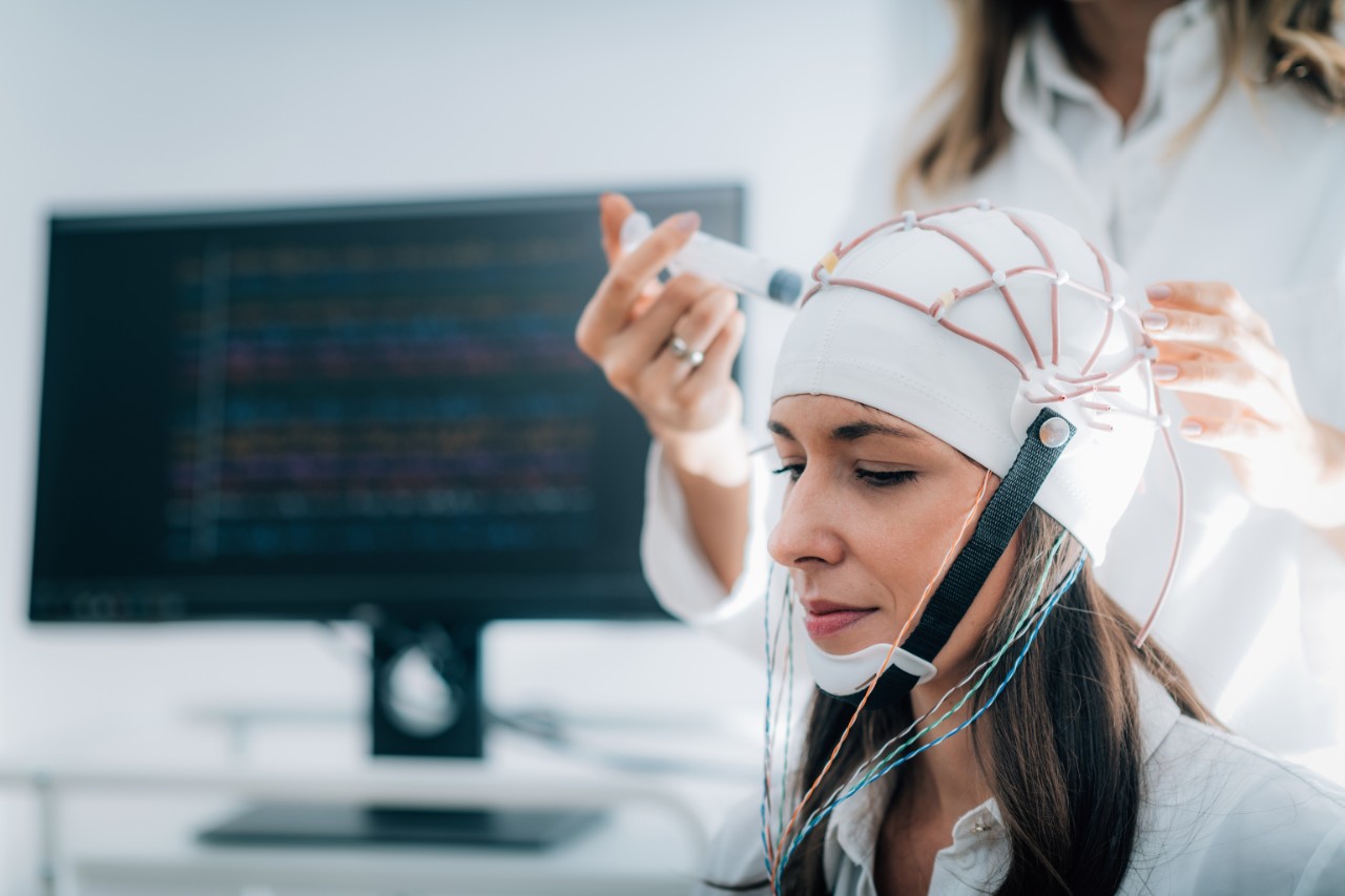 a woman in a medical office with a brain monitoring device on her head, it looks like a white skullcap with lots of wires