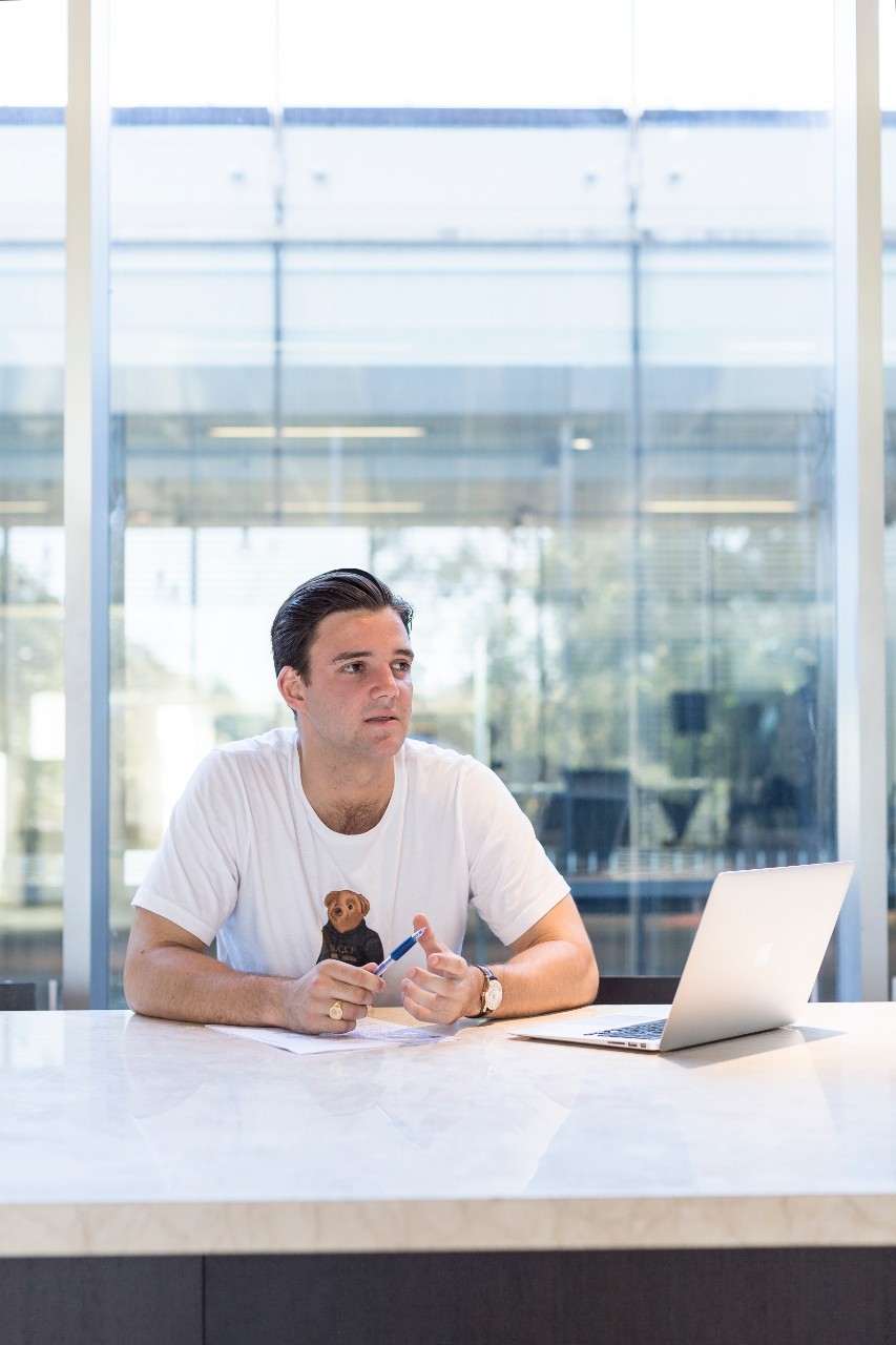 Commerce student Duncan sitting on a chair behind a desk