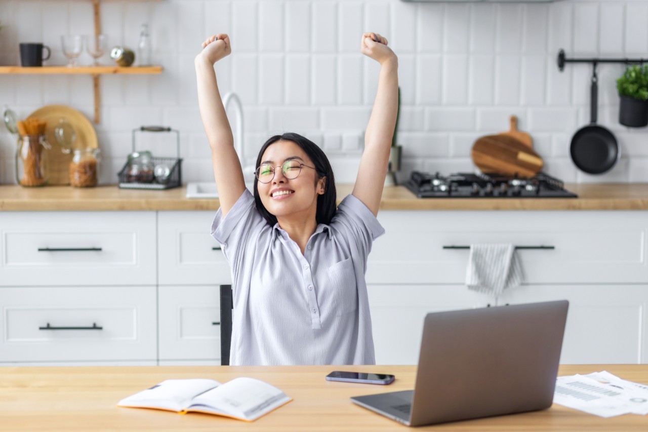a woman sitting at her laptop stretching her arms above her head