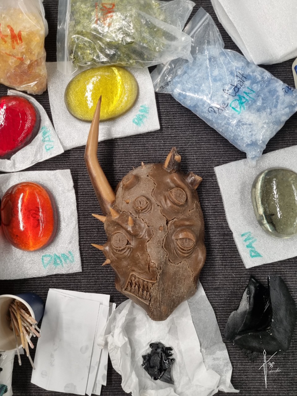 An unfinished clay mask surrounded by pieces of colourful glass