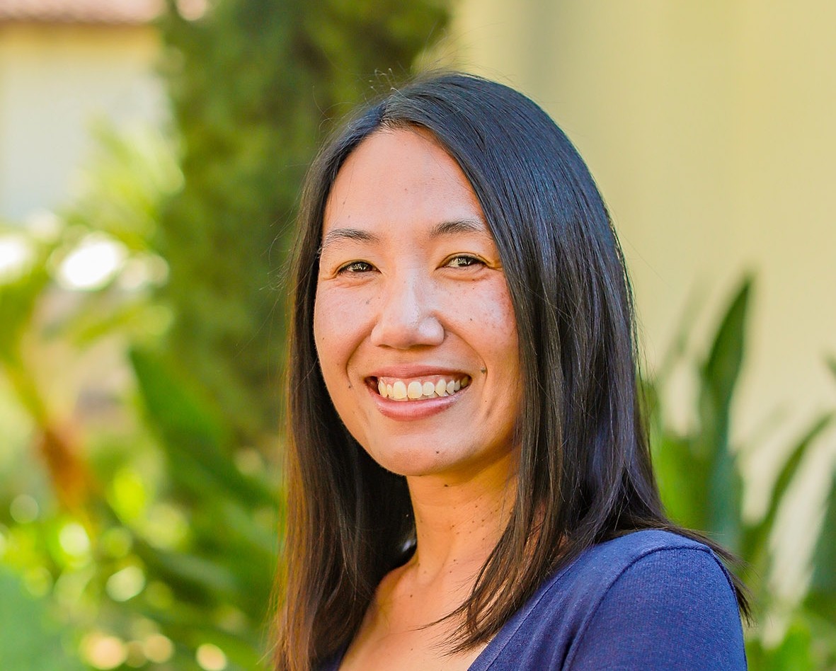 A woman dressed in a blue dress is standing side on looking at the camera