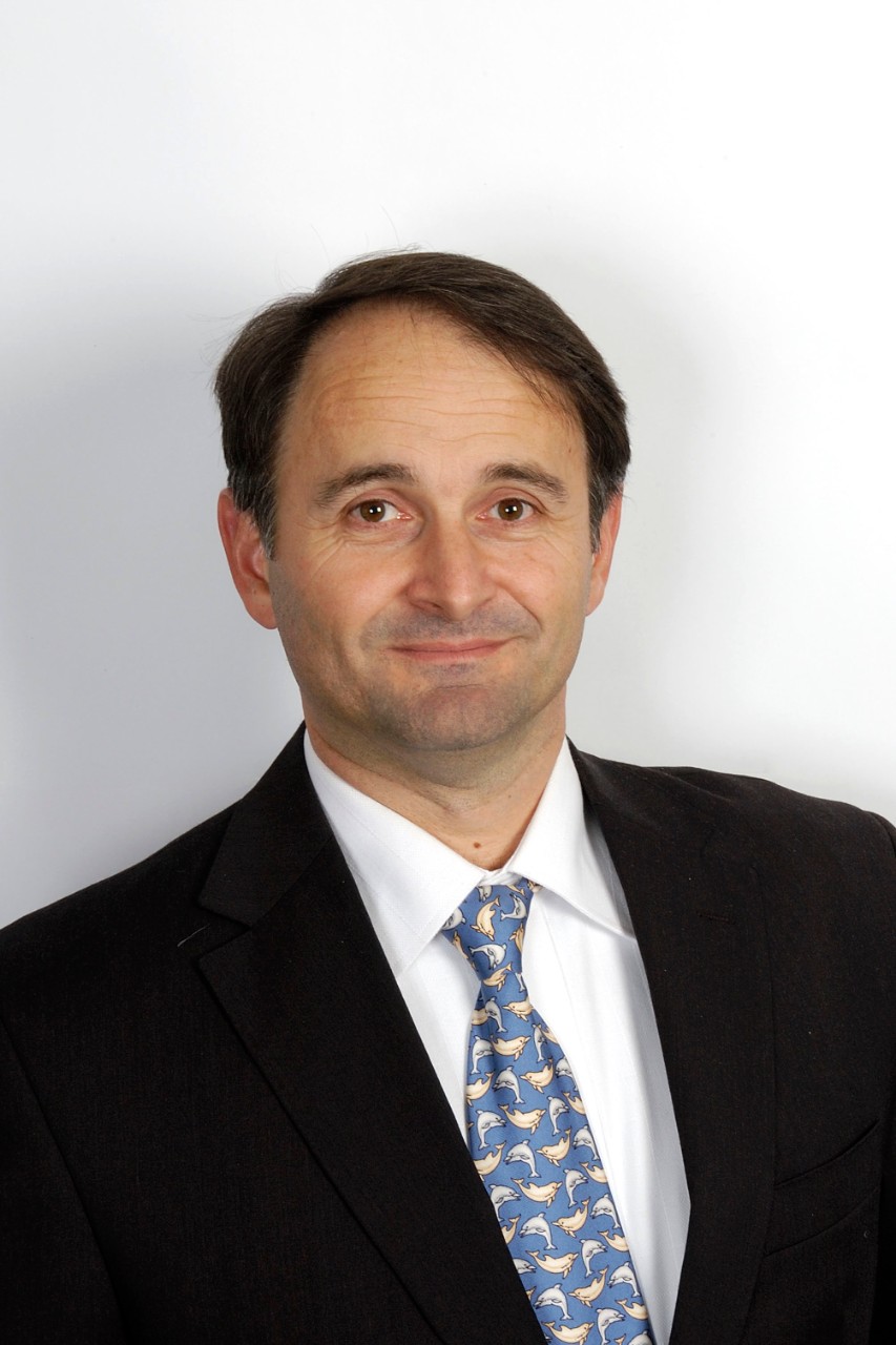 University of Sydney graduate Peter Pontikis's professional headshot portrait of man dressed in black and white buisness suit and a blue tie with light blue and yellow-coloured dolphin pattern