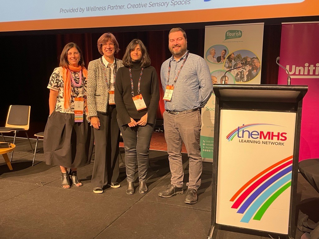 four people stand on a stage at a conference.