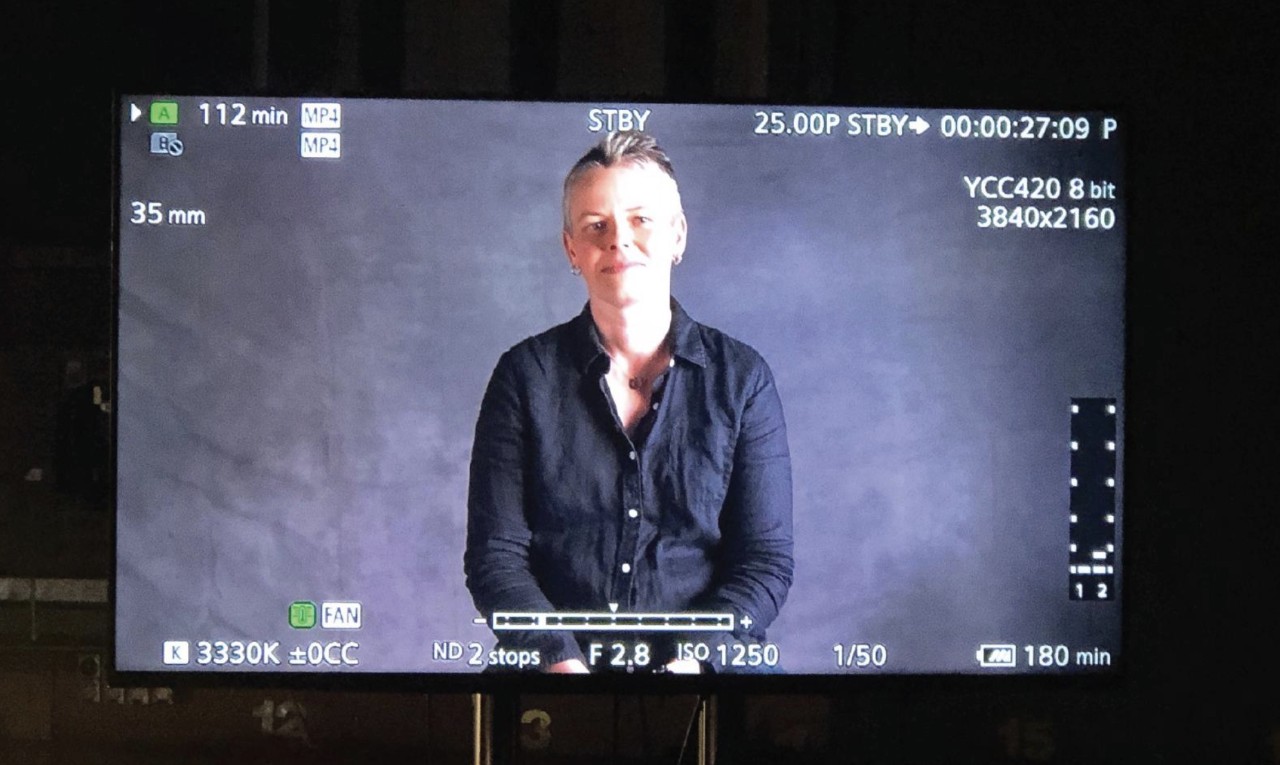 A white woman with blonde hair on a tv screen in a purple background. 