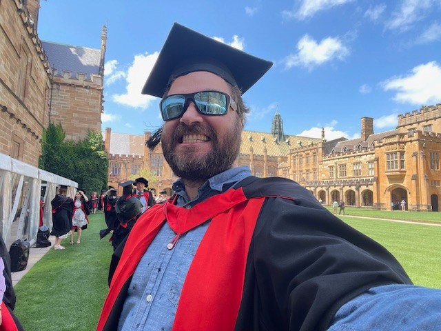 Matthew Sunderland standing in graduation gear in the University of Sydney quad. 