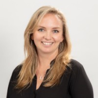 A photo of Emma Barrett. She is a blonde haired woman wearing a black shirt. She is smiling. 