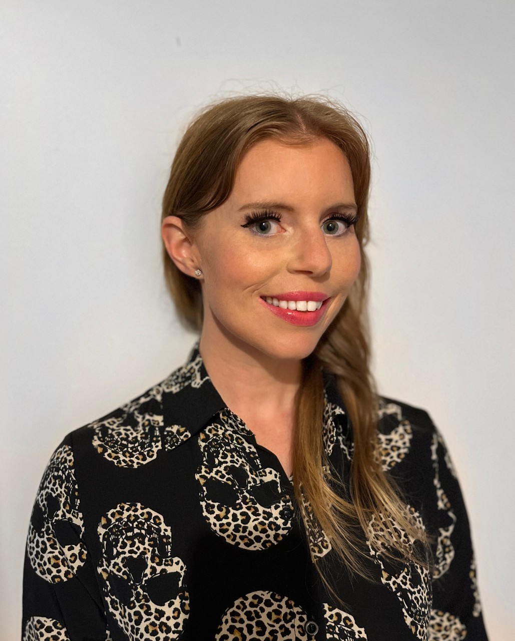 Jasmin has long blonde-brown hair, is wearing red lipstick and is wearing a black shirt. 