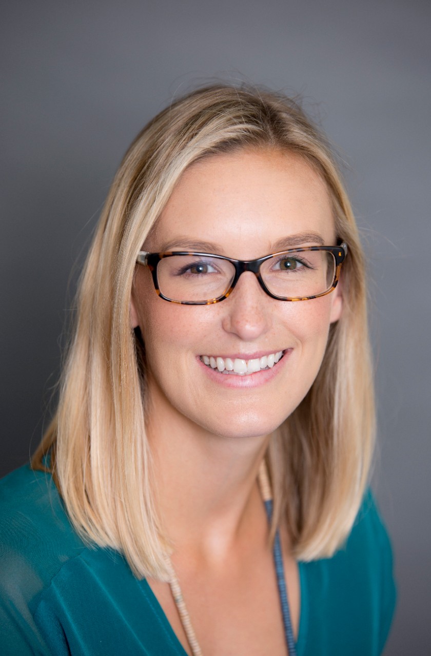 An image of Louise Birrell. She is a blonde haired woman wearing a green shirt and black glasses. She is smiling.