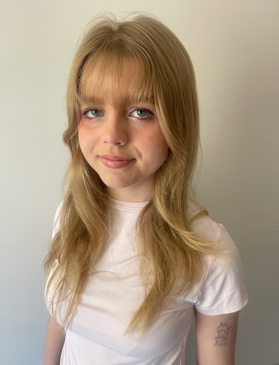 A woman looking directly ahead. She has long blonde hair, a long fringe and is wearing a white shirt. 