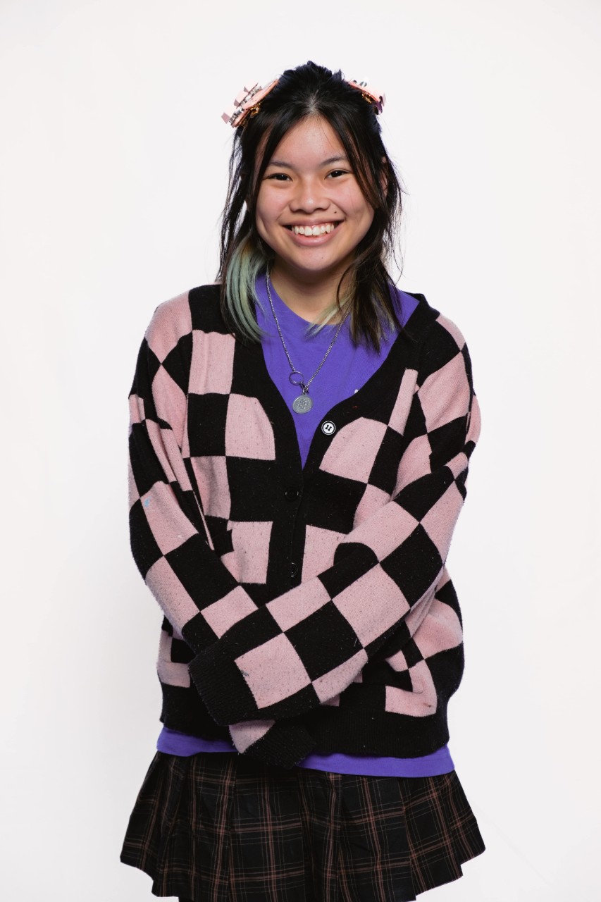 A person with shoulder length dark hair and is wearing a black and white check jumper. 