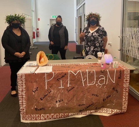 photo of three women from Pacific Islands heritage wearing flowers on their head standing at a table for vaccines