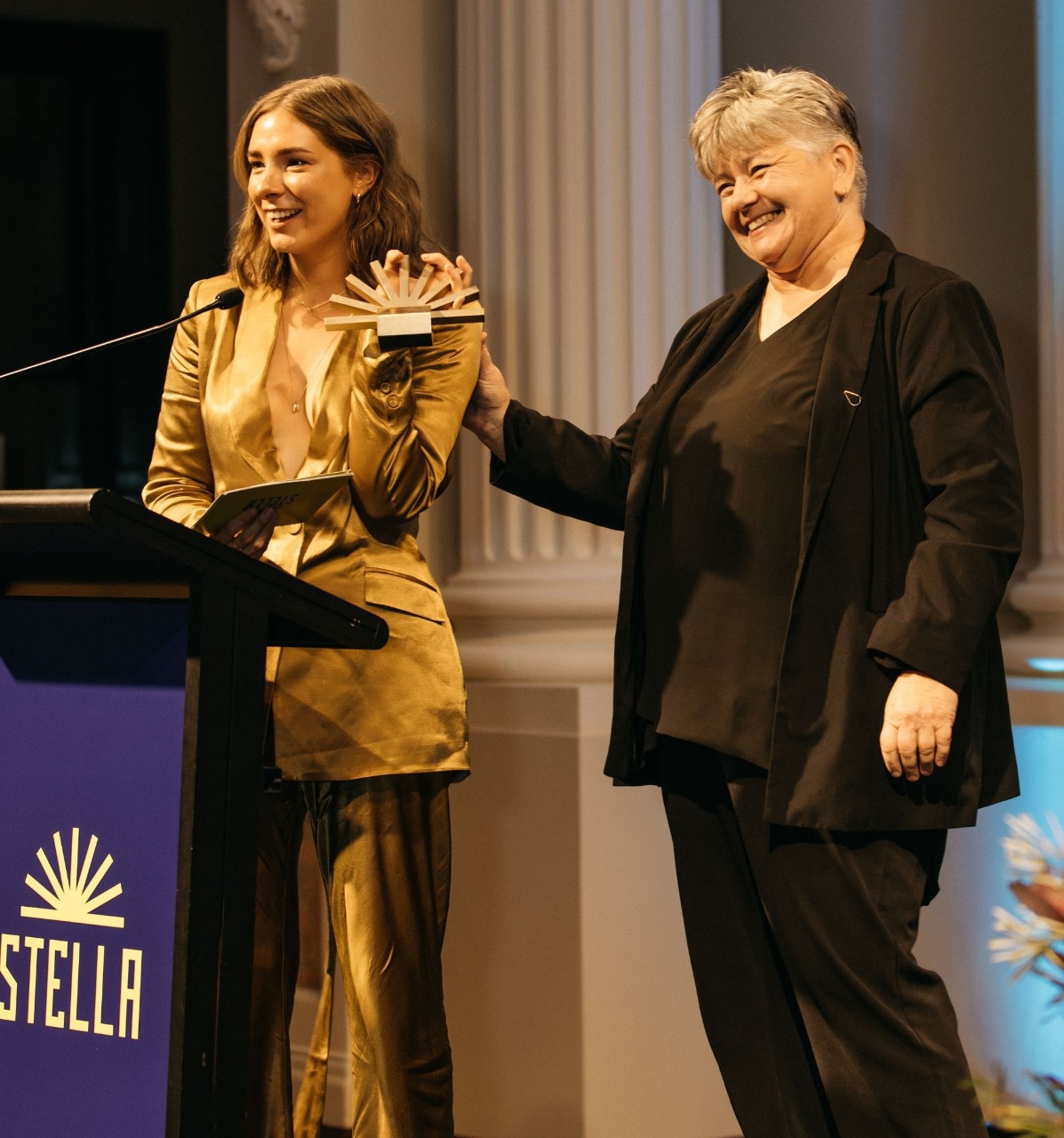 photo of Evelyn Araluen wearing a gold suit holding her gold trophy in the air 