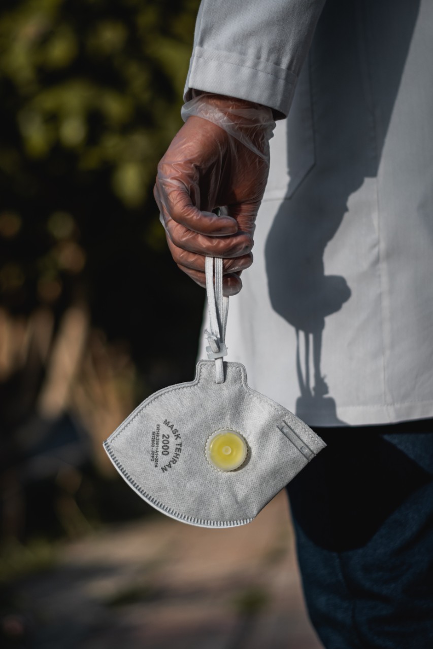 A doctor holding a medical face mask in a gloved hand 