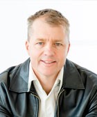 a man wearing a leather jacket looks at the camera and smiles