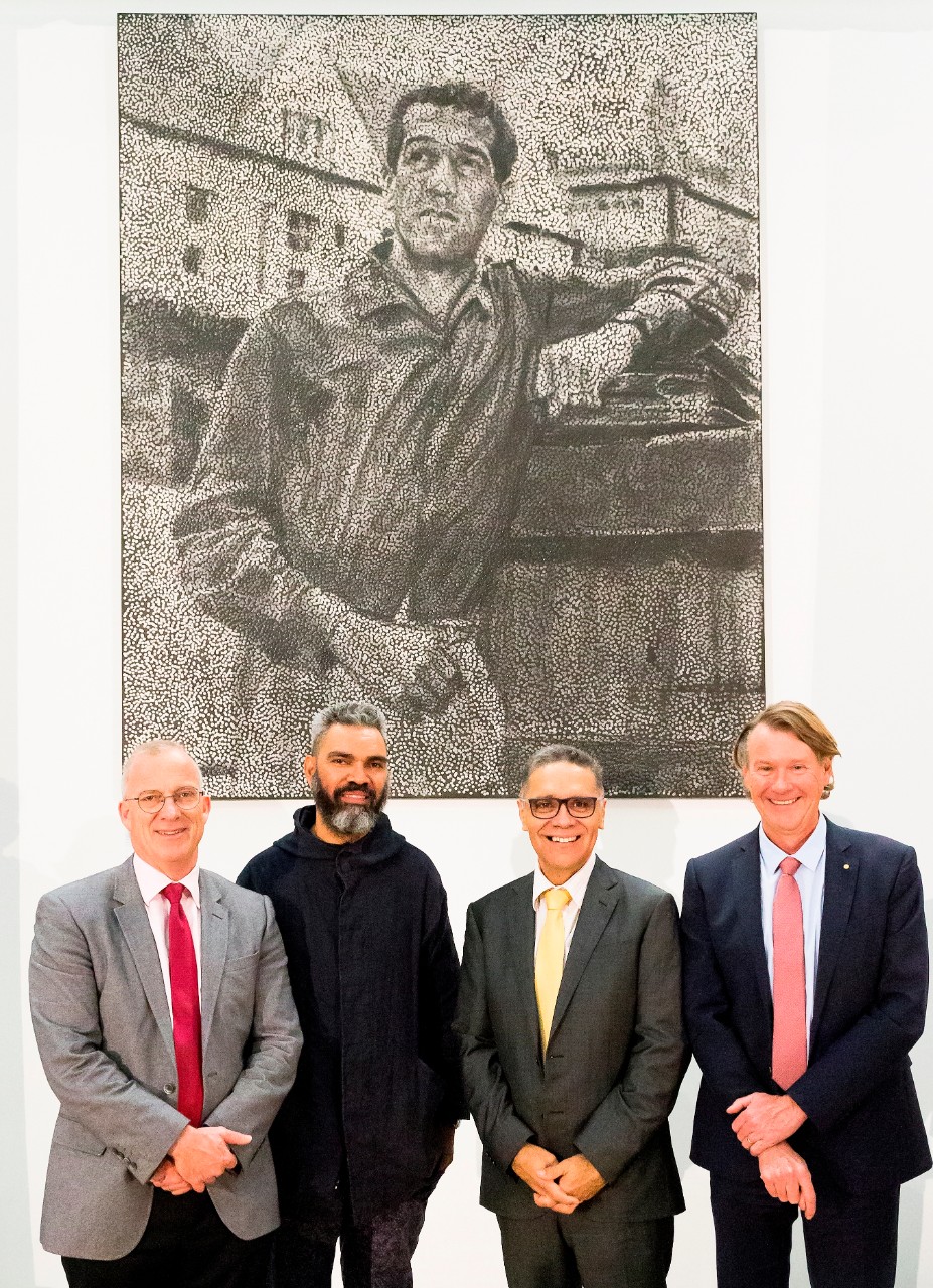 A photo of people standing in front of a black and white dot painting of Charles Perkins