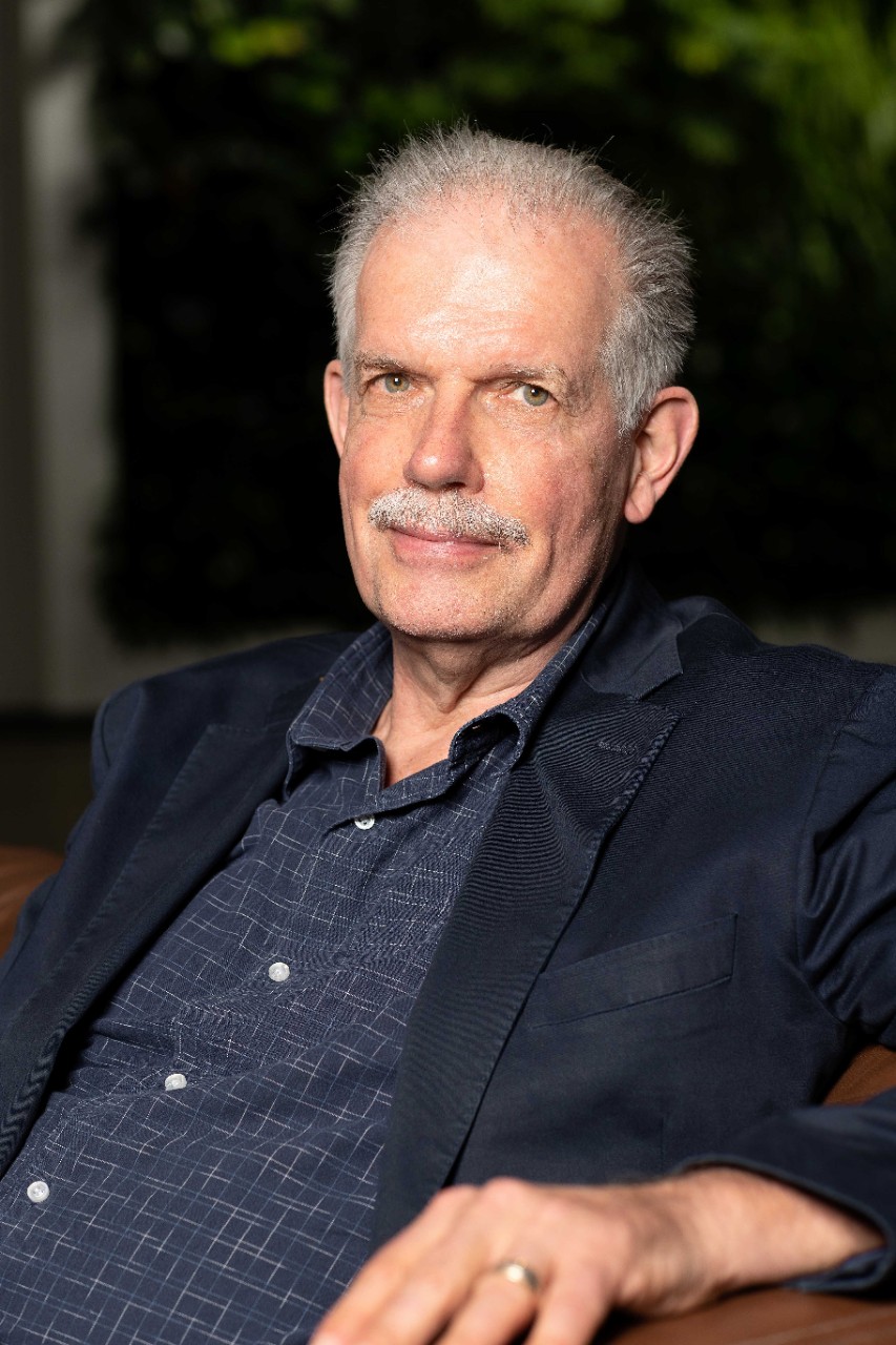Photo of Neil Smith in a black shirt and black background smiling at the camera