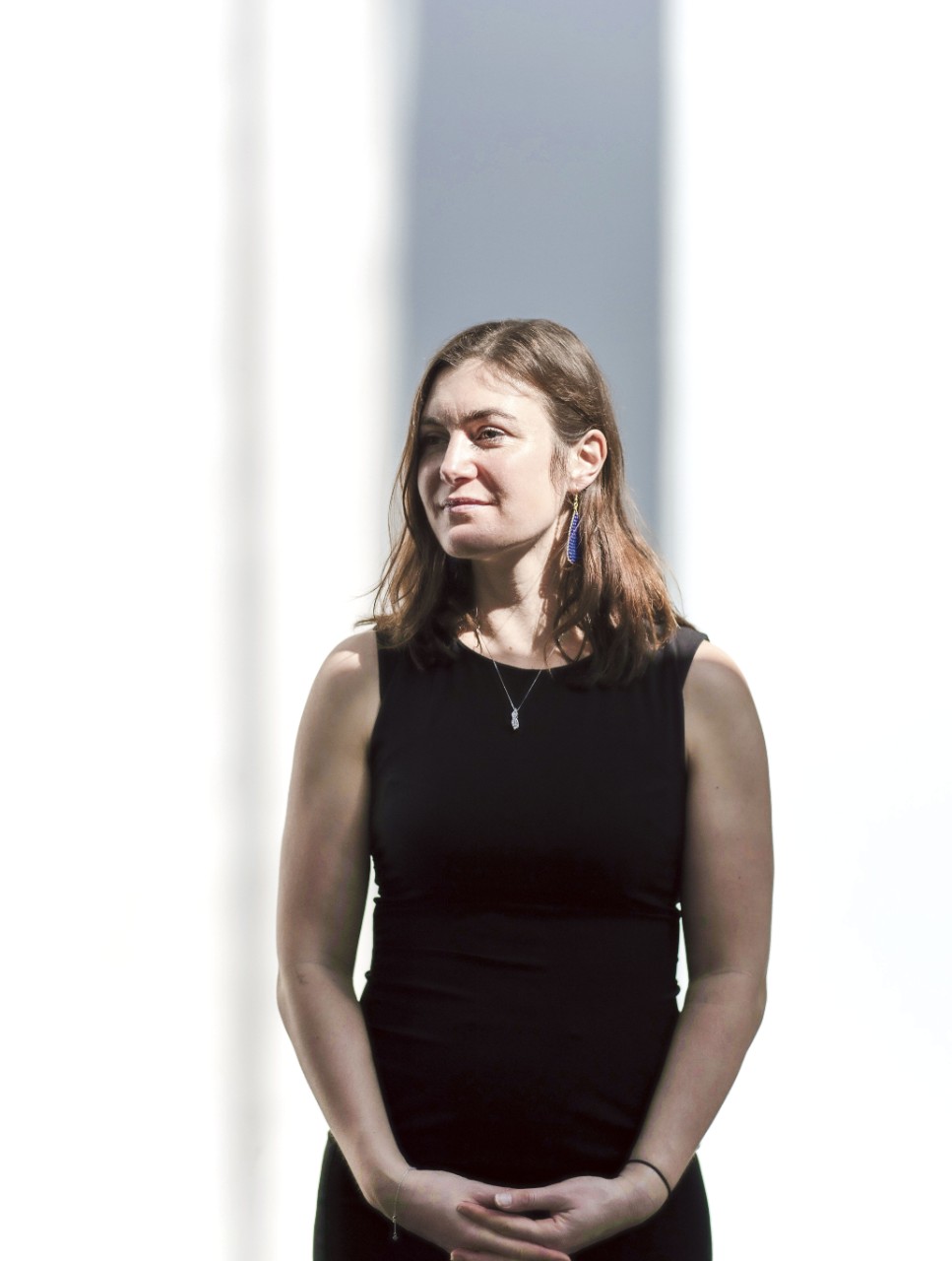 A contemplative Sarah McDonald, with hands cupped in front of her, in a brightly lit room with dramatic shadows behind.