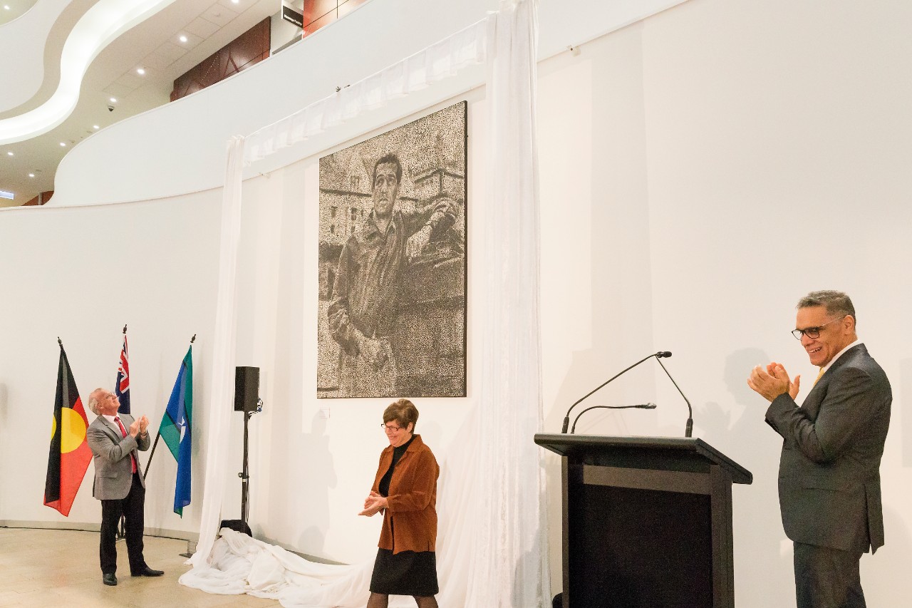A photo of people in front of a black and white dot painting of Charles Perkins.